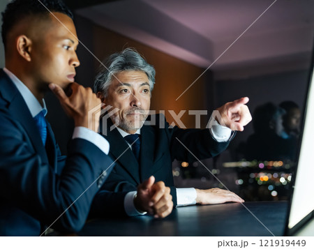 夜のオフィスで画面を見ながら会議する多国籍ビジネスパーソン 夜のオフィスで画面を見ながら会議する多国籍ビジネスパーソン 121919449