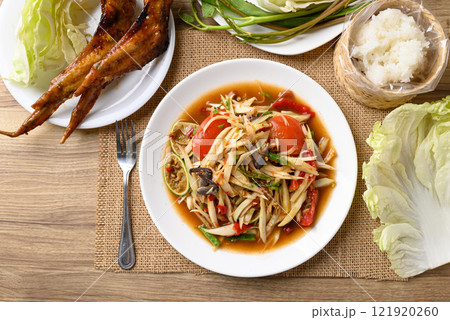 Spicy papaya salad (Som Tum) eating with sticky rice and grilled chicken wing on wooden table 121920260