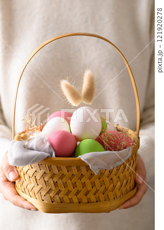 White easter eggs with bunny rabbit ears and colorful easter eggs in basket holding by hand White easter eggs with bunny rabbit ears and colorful easter eggs in basket holding by hand 121920278