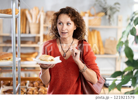Happy female customer tries delicious bocadillo in bakery interior 121921579