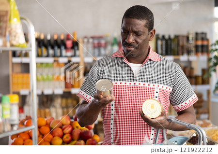 Adult man choosing canned food in grocery store 121922212