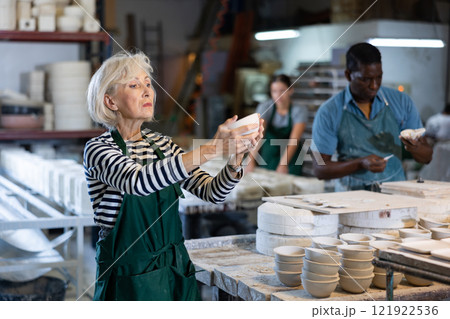 Portrait of positive senior woman holding ceramic cups at workshop 121922536