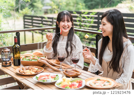 テラスで食事・バーベキュー・ホームパーティー・グランピングする若い女性・友達 121923476