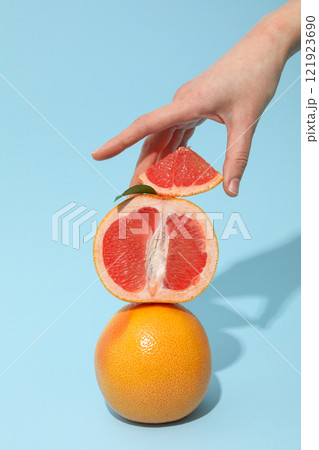Sliced and whole grapefruit in female hand on blue background 121923690