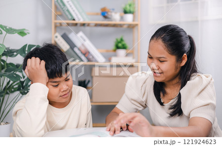 Teacher or sister helping boy writing lesson and learning to write; Female tutor helping little elementary school boy with homework during individual lesson at home; Education home school concept. 121924623