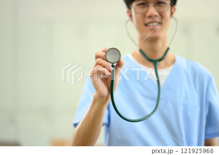 Smiling medical student in scrubs holding a stethoscope towards the camera Smiling medical student in scrubs holding a stethoscope towards the camera 121925968