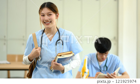 Smiling medical student in scrubs carrying books heading to class 121925974