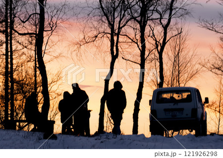 Picnic in nature by car at the top of a mountain in winter at sunset, silhouettes of people and a car on a yellow background Silhouetted figures stand against a stunning and beautiful sunset at days Picnic in nature by car at the top of a mountain in winter at sunset, silhouettes of people and a car on a yellow background Silhouetted figures stand against a stunning and beautiful sunset at days 121926298