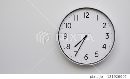 Minimalist Analog Wall Clock with White Face and Simple Black Hands Showing 19.35/07.35 - Ideal for Time Management and Modern Decor Concepts 121926995