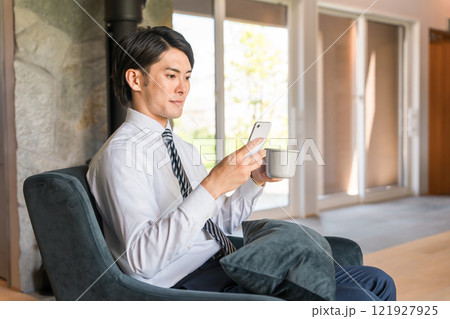 家でスマホ・スマートフォンを見るビジネスマン（ニュース・電子書籍・読書・アプリ・スケジュール） 121927925