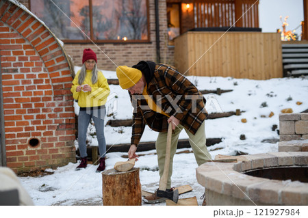 Elderly man is chopping wood outside. He is preparing logs for the fireplace. Elderly man is chopping wood outside. He is preparing logs for the fireplace. 121927984