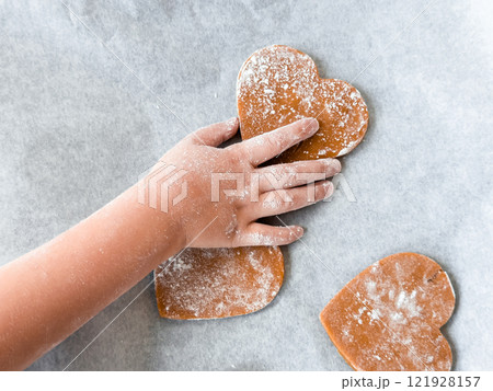 Childs hand decorating heart shaped cookies on baking sheet 121928157