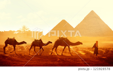Horizontal banner with caravan of camels and Great Pyramids of Chephren and Cheops, Cairo, Egypt. Man with three dromedary in two pyramids, Giza complex (Giza Necropolis). On sunrise sky background 121928578