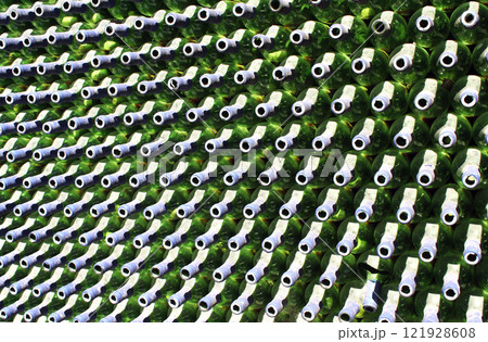 Full frame wall with empty green beer bottles necks. Alcohol theme. Endless rows of wine bottles. Green glass bottle wall with sunlight from behind 121928608