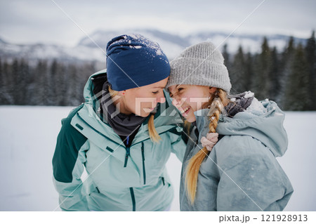 Mom and cute girl hugging, standing in the middle of snowy nature. 121928913