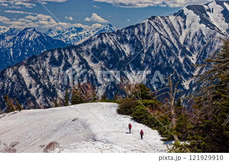 残雪の爺ヶ岳南尾根を行く登山者と槍・穂高連峰の眺め 121929910