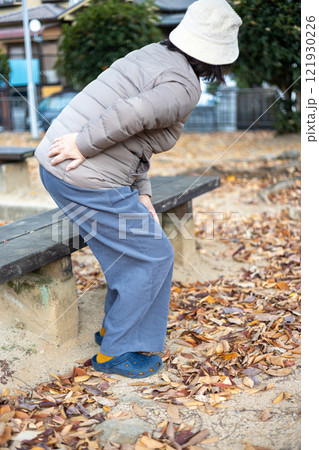 公園のベンチから立ち上がった腰と膝の痛そうなシニア女性 121930226