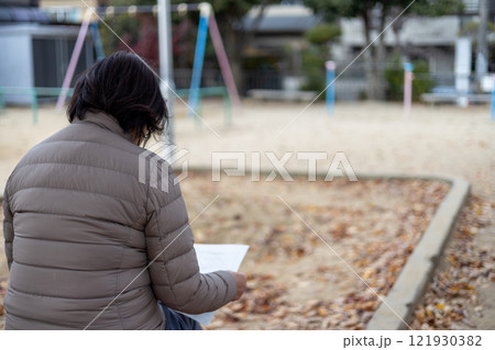 ポツンと公園のベンチに座って紙切れを見ているシニア女性 121930382