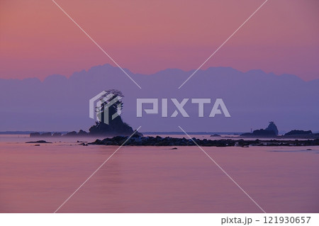 薄紫色の朝焼け空と立山連峰剱岳を背景にした富山湾雨晴海岸の風景 121930657