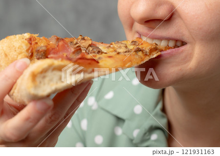 A young woman enjoying a slice of pizza with toppings, smiling and holding it close to her mouth. 121931163