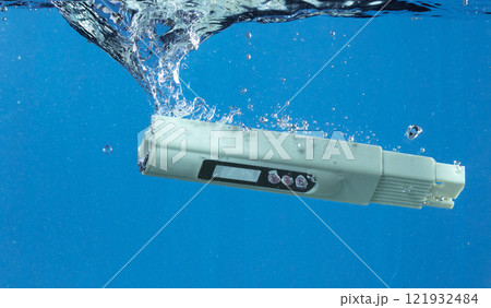 PH acid level test Device tools on quality water on screen. PH acid level tester device tools fall under water splashing splattering with air bubble over blue background isolated 121932484