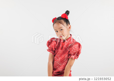 Smiling Asian girl in vibrant red festive traditional dress with matching hair accents, isolated white background. Her joyful expression embodies holiday celebration 121933052