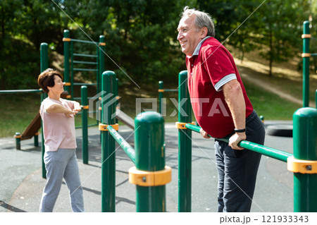 Elderly man doing exercises on a horizontal bar at an outdoor sports ground 121933343