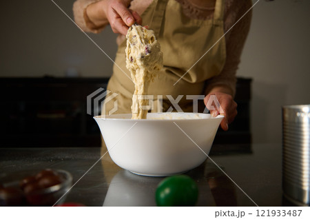 Baker preparing dough in a white bowl wearing an apron and evening light Baker preparing dough in a white bowl wearing an apron and evening light 121933487