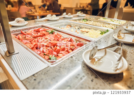 Buffet bar or buffet in the cafe. A metal container with sliced fresh tomatoes. Against the background of unrecognizable people dining. High quality photo Buffet bar or buffet in the cafe. A metal container with sliced fresh tomatoes. Against the background of unrecognizable people dining. High quality photo 121933937