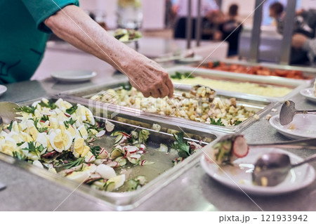 The hand of an unrecognizable volunteer puts nutritious food on a plate in a modern charity canteen. High quality photo The hand of an unrecognizable volunteer puts nutritious food on a plate in a modern charity canteen. High quality photo 121933942