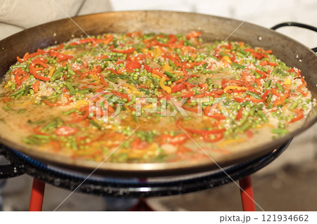 Cooking paella in a large metal frying pan. A traditional Spanish dish with rice and vegetables. Cooking paella in a large metal frying pan. A traditional Spanish dish with rice and vegetables. 121934662