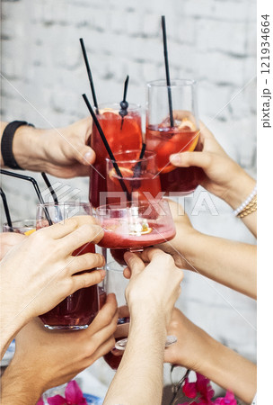 Close-up of male and female hands with elegant glasses. Men and women toast with goblets of delicious fragrant cocktails. Friends clink glasses with tasty drinks. 121934664