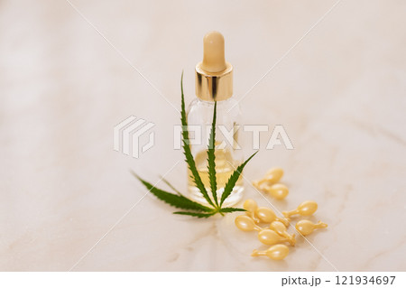Mockup bottle of cosmetic product with cannabis leaves on beige background. Yellow capsules with whitening moisturizing facial serum with hyaluronic acid with hemp leaf on marble table. 121934697