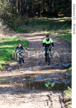 Father and son mountain biking on a muddy trail through a forest. Father and son mountain biking on a muddy trail through a forest. 121934892