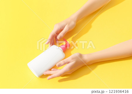 Womans hands holding white bottle on yellow background. Beauty treatment concept. 121936416