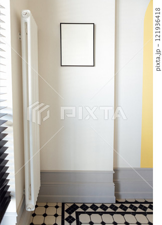 Stylish modern interior of the room with white walls and contrasting tiles. A mockup for a poster with a black wooden frame. Stylish modern interior of the room with white walls and contrasting tiles. A mockup for a poster with a black wooden frame. 121936418