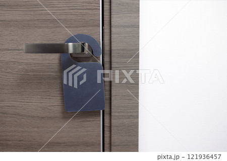 Close-up of a closed wooden door of a hotel room with an empty black sign. The layout of the sign on the modern door handle. Close-up of a closed wooden door of a hotel room with an empty black sign. The layout of the sign on the modern door handle. 121936457