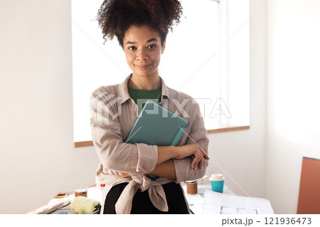 Attractive smiling African woman holds tablet and coffee and checks house plan 121936473