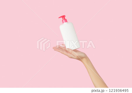 Womans hand holding white bottle on pastel pink background 121936495