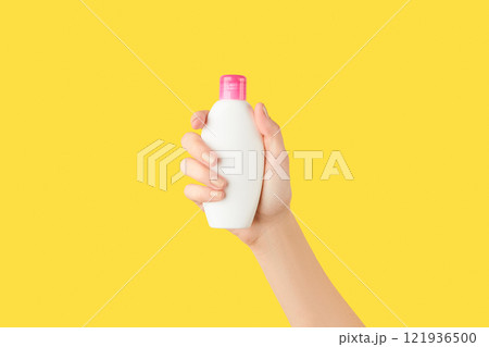Womans hand holding white bottle on yellow background. Self care concept. 121936500