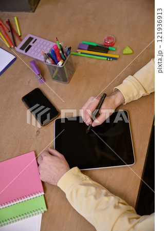 Focused image of person using stylus on tablet with surrounding stationery, symbolizing creativity and technology integration. Focused image of person using stylus on tablet with surrounding stationery, symbolizing creativity and technology integration. 121936913