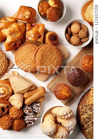 Assorted baked goods displayed on a wooden table, featuring cookies, pastries, and muffins in a cozy setting Assorted baked goods displayed on a wooden table, featuring cookies, pastries, and muffins in a cozy setting 121937209