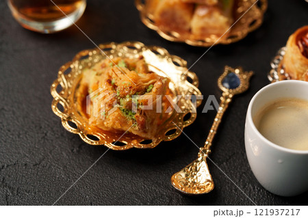 Delightful dessert with sweet pastries and coffee served in golden bowls on a dark table Delightful dessert with sweet pastries and coffee served in golden bowls on a dark table 121937217
