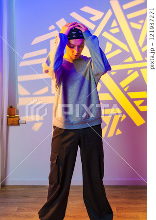 A young person stands with their hands on their head, looking down, in front of a wall with a projected pattern 121937271