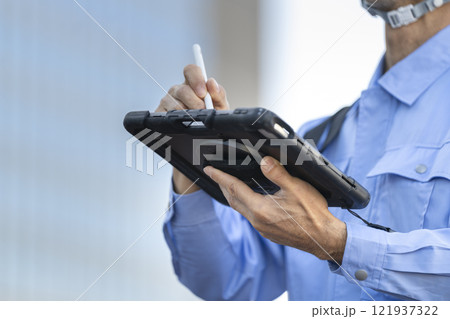タブレットに入力する作業服姿の男性の手元　 121937322