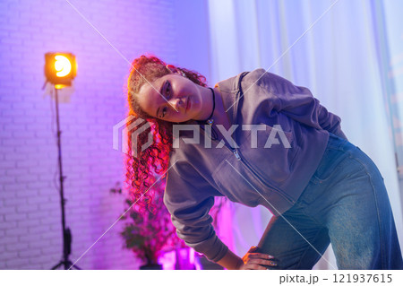A young woman with pink hair poses in a studio, lit by a bright light 121937615