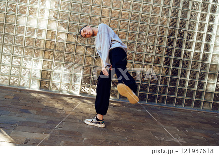 A young man dances in front of a glass block wall, showcasing his unique style and impressive moves 121937618