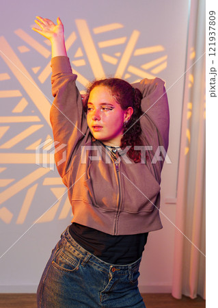 A young woman with curly hair poses in a studio, illuminated by colorful lights A young woman with curly hair poses in a studio, illuminated by colorful lights 121937809