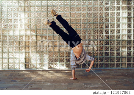 A young man performs a handstand in front of a brick wall 121937862
