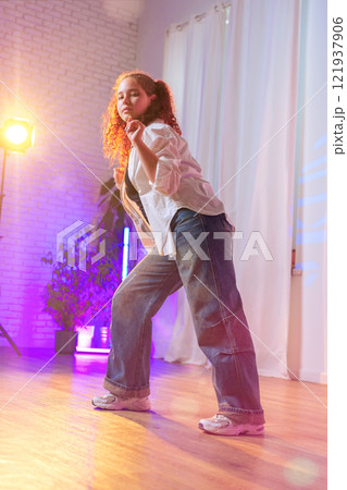 A young woman with curly red hair dances in a studio lit with colored lights 121937906